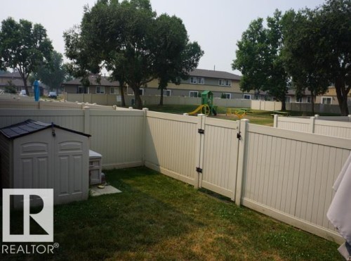 Fenced backyard featuring a storage shed and a gated entry to a common green space with mature trees - #38 8930 99 Av, Fort Saskatchewan, AB - Outdoor