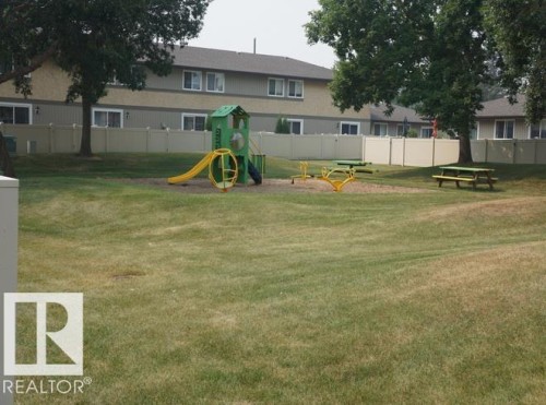 Expansive grassy area featuring a playground structure with a slide, a seesaw, and a picnic table - #38 8930 99 Av, Fort Saskatchewan, AB - Outdoor