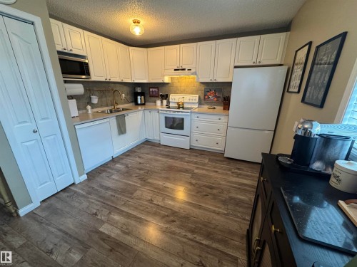 Kitchen featuring white cabinetry, light countertops, subway tile backsplash, wood-finish flooring, and a built-in microwave - #38 8930 99 Av, Fort Saskatchewan, AB - Indoor Photo Showing Kitchen With Double Sink