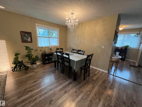 Wood-finish flooring, overhead crystal chandelier, and a large window with white trim - #38 8930 99 Av, Fort Saskatchewan, AB - Indoor Photo Showing Dining Room
