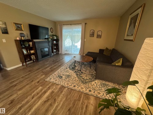 Wood-finish flooring throughout, featuring a fireplace with a dark mantel, and recessed ceiling lighting - #38 8930 99 Av, Fort Saskatchewan, AB - Indoor Photo Showing Living Room