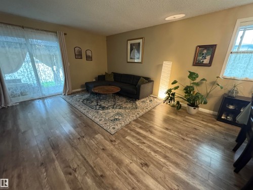 Wood-finish flooring throughout, complemented by warm-toned wall finishes and a sliding glass door - #38 8930 99 Av, Fort Saskatchewan, AB - Indoor Photo Showing Living Room With Fireplace