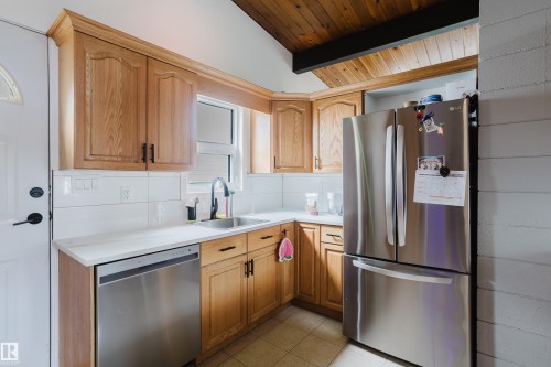 Light wood-finish cabinetry, white countertops, stainless steel appliances, white subway tile backsplash, and a wood-paneled vaulted ceiling - 9059 52 Street Nw, Edmonton, AB - Indoor Photo Showing Kitchen