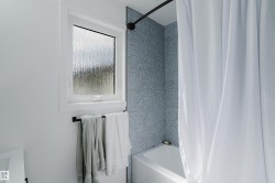 White bathtub with a curved shower rod, patterned blue-gray wall tile, and a privacy window - 