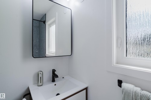 White vanity with a rectangular sink, matte black faucet, and a rectangular mirror with a black frame - 9059 52 Street Nw, Edmonton, AB - Indoor Photo Showing Bathroom