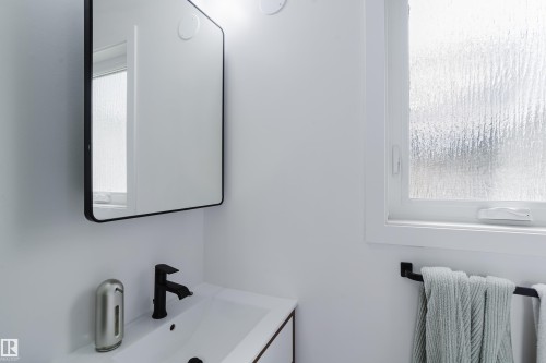 Wall-mounted rectangular mirror with a black frame, matte black faucet, integrated sink, and privacy glass window - 9059 52 Street Nw, Edmonton, AB - Indoor Photo Showing Bathroom