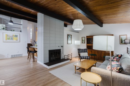 Exposed wood beam ceiling, wood-finish flooring, tiled fireplace with hearth, built-in shelving, and white walls - 9059 52 Street Nw, Edmonton, AB - Indoor Photo Showing Living Room With Fireplace