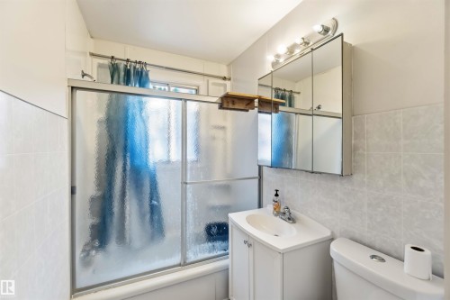 Bathroom featuring a white vanity with integrated sink, a mirrored medicine cabinet, and a shower/tub combination with sliding frosted glass doors - 12243 104 Street Nw, Edmonton, AB - Indoor Photo Showing Bathroom