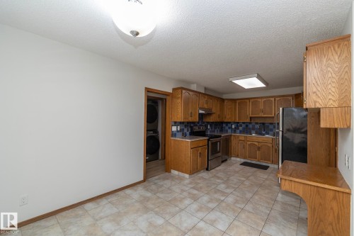 Kitchen featuring wood cabinetry, tile flooring, stainless steel appliances, and a blue tile backsplash - 11138 30 Avenue Nw, Edmonton, AB - Indoor Photo Showing Kitchen