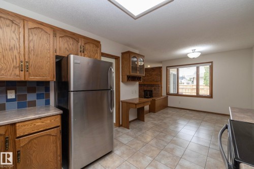 Stainless steel refrigerator, wood-finish cabinetry, tiled backsplash, tiled flooring, built-in display cabinet with wine rack, and a skylight - 11138 30 Avenue Nw, Edmonton, AB - Indoor Photo Showing Kitchen