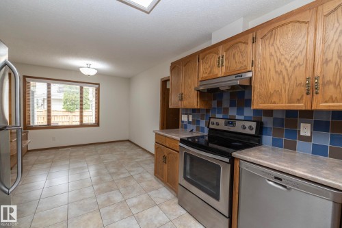 Kitchen featuring tile flooring, wood cabinetry, stainless steel appliances, a tiled backsplash, and an overhead skylight - 11138 30 Avenue Nw, Edmonton, AB - Indoor Photo Showing Kitchen