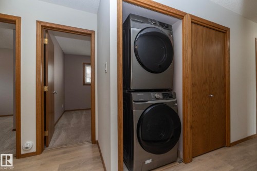 Stackable washer and dryer, wood-finish flooring, wood-paneled doors, and painted walls - 11138 30 Avenue Nw, Edmonton, AB - Indoor Photo Showing Laundry Room