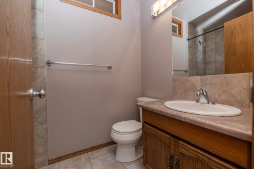 Vanity with integrated sink, wood-finish cabinetry, neutral countertop, and tiled flooring - 11138 30 Avenue Nw, Edmonton, AB - Indoor Photo Showing Bathroom