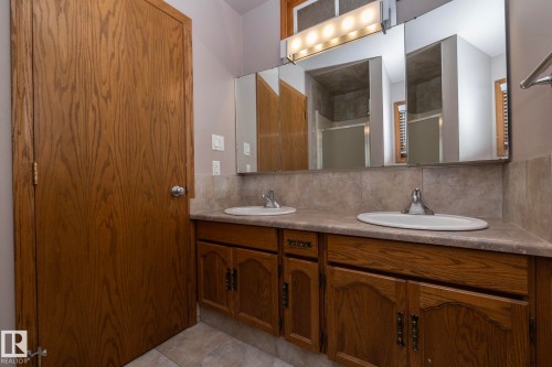 Double vanity with wood-finish cabinetry, integrated sinks, chrome faucets, and a full-width mirror - 11138 30 Avenue Nw, Edmonton, AB - Indoor Photo Showing Bathroom