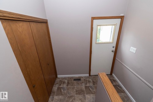 Wood-look bi-fold closet doors, white exterior door with window, and a wood-finish handrail - 11138 30 Avenue Nw, Edmonton, AB - Indoor Photo Showing Other Room