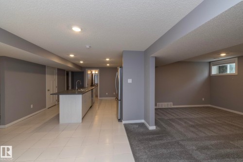 Spacious open-concept lower level featuring a central island with sink, stainless steel refrigerator, recessed lighting, and a window for natural light - 11138 30 Avenue Nw, Edmonton, AB - Indoor