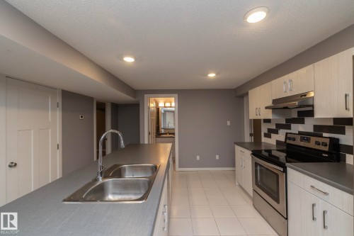 Stainless steel double basin sink, stainless steel appliances, light wood-finish cabinetry, tile flooring, and a patterned tile backsplash - 11138 30 Avenue Nw, Edmonton, AB - Indoor Photo Showing Kitchen With Stainless Steel Kitchen With Double Sink