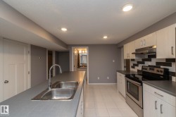 Stainless steel double basin sink, stainless steel appliances, light wood-finish cabinetry, tile flooring, and a patterned tile backsplash - 