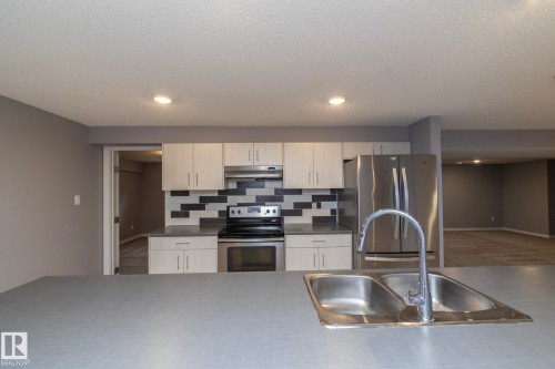 Kitchen featuring a double basin stainless steel sink, stainless steel appliances, light-toned cabinetry, and a patterned tile backsplash - 11138 30 Avenue Nw, Edmonton, AB - Indoor Photo Showing Kitchen With Stainless Steel Kitchen With Double Sink