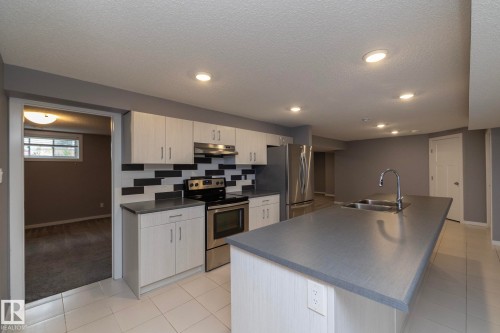 Kitchen featuring stainless steel appliances, dual basin sink, integrated island, and mosaic tile backsplash - 11138 30 Avenue Nw, Edmonton, AB - Indoor Photo Showing Kitchen With Double Sink
