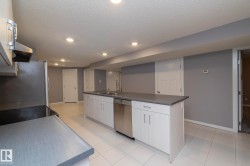 Kitchen island with integrated sink, stainless steel dishwasher, light wood-finish cabinetry, and recessed lighting - 