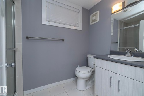 White tile flooring, single vanity with light-toned cabinetry, stainless steel fixtures, mirror, and enclosed shower - 11138 30 Avenue Nw, Edmonton, AB - Indoor Photo Showing Bathroom