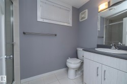 White tile flooring, single vanity with light-toned cabinetry, stainless steel fixtures, mirror, and enclosed shower - 