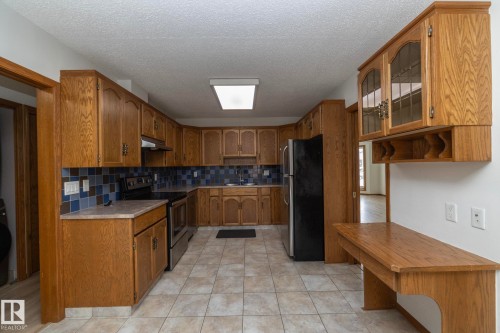 Wood-finish cabinetry, tile flooring, blue tile backsplash, built-in desk, and stainless steel appliances - 11138 30 Avenue Nw, Edmonton, AB - Indoor Photo Showing Kitchen