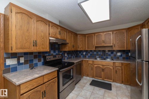 Kitchen featuring wood cabinetry, stainless steel appliances, patterned tile backsplash, and light-toned countertops - 11138 30 Avenue Nw, Edmonton, AB - Indoor Photo Showing Kitchen With Stainless Steel Kitchen With Double Sink