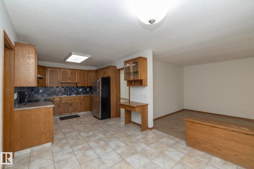 Kitchen with wood-finish cabinetry, tile flooring, and a stainless steel refrigerator - 11138 30 Avenue Nw, Edmonton, AB - Indoor Photo Showing Kitchen