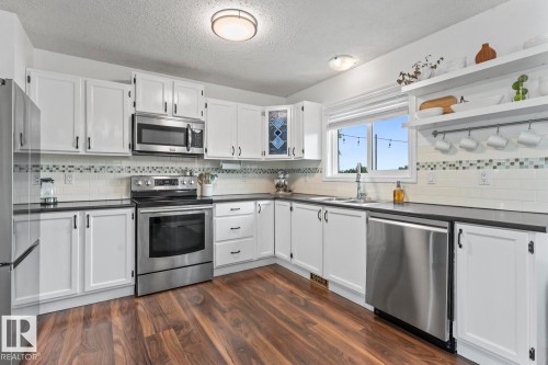 White cabinetry with dark hardware, stainless steel appliances, dark countertops, wood-finish flooring, and white subway tile backsplash - 5330 43 Street, Cold Lake, AB - Indoor Photo Showing Kitchen With Stainless Steel Kitchen With Double Sink