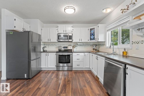 Kitchen featuring white cabinetry, wood-finish flooring, stainless steel appliances, dual basin sink, and a multi-tone tile backsplash - 5330 43 Street, Cold Lake, AB - Indoor Photo Showing Kitchen With Stainless Steel Kitchen With Double Sink
