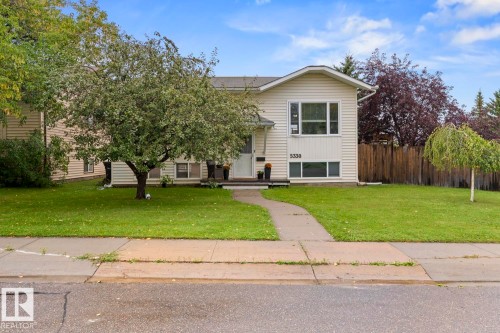 Cream-colored exterior siding with white trim, a concrete walkway, mature trees, and a wooden privacy fence - 5330 43 Street, Cold Lake, AB - Outdoor