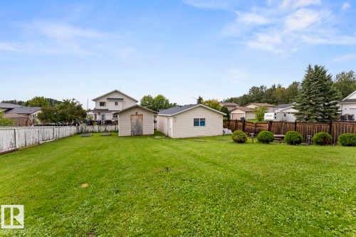 Expansive grassy yard area featuring two storage sheds and a wood fence - 5330 43 Street, Cold Lake, AB - Outdoor