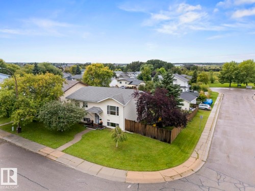 Corner lot residence featuring a light-colored exterior, an asphalt shingle roof, mature perimeter trees, and a wooden fence - 5330 43 Street, Cold Lake, AB - Outdoor With View