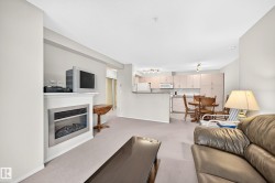 Integrated living area with a built-in fireplace, neutral carpeting, and a kitchen featuring light cabinetry, a tile backsplash, and stainless-steel appliances - 