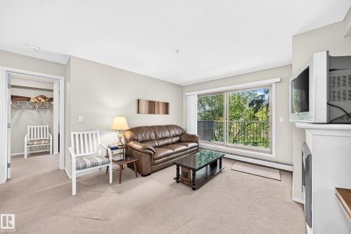 Light-colored wall paint and carpeting, large sliding glass door, built-in wall unit, and a doorway opening to a closet - #216 17003 67 Av Nw, Edmonton, AB - Indoor Photo Showing Living Room