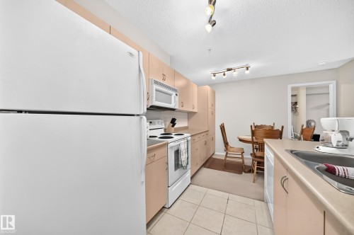 Functional kitchen featuring light wood-finish cabinetry, white appliances, and tiled flooring - #216 17003 67 Av Nw, Edmonton, AB - Indoor Photo Showing Kitchen