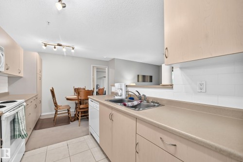 Kitchen featuring light wood-finish cabinetry, white subway tile backsplash, durable countertops, and a built-in dishwasher - #216 17003 67 Av Nw, Edmonton, AB - Indoor Photo Showing Kitchen With Double Sink