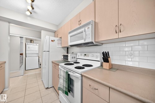 Functional kitchen featuring a full suite of white appliances, light wood-finish cabinetry, and a white subway tile backsplash - #216 17003 67 Av Nw, Edmonton, AB - Indoor Photo Showing Kitchen