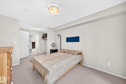 Carpeted flooring, light neutral wall paint, recessed lighting, white interior doors, and a partial bathroom with a toilet and shower enclosure - #216 17003 67 Av Nw, Edmonton, AB - Indoor Photo Showing Bedroom