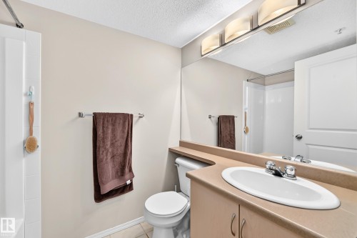 White vanity with an integrated sink and chrome faucet, full-width mirror, and overhead four-light fixture - #216 17003 67 Av Nw, Edmonton, AB - Indoor Photo Showing Bathroom