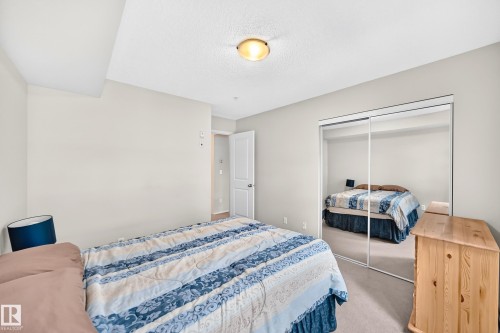 Mirrored closet doors, light neutral walls, recessed ceiling light, and light-toned carpeting - #216 17003 67 Av Nw, Edmonton, AB - Indoor Photo Showing Bedroom
