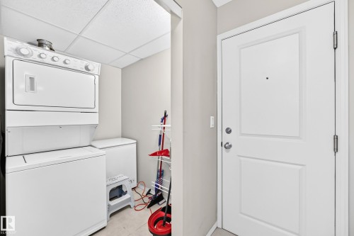 Laundry area featuring a stacked washer and dryer, an additional white appliance, and light-toned flooring - #216 17003 67 Av Nw, Edmonton, AB - Indoor Photo Showing Laundry Room