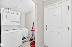 Laundry area featuring a stacked washer and dryer, an additional white appliance, and light-toned flooring - 