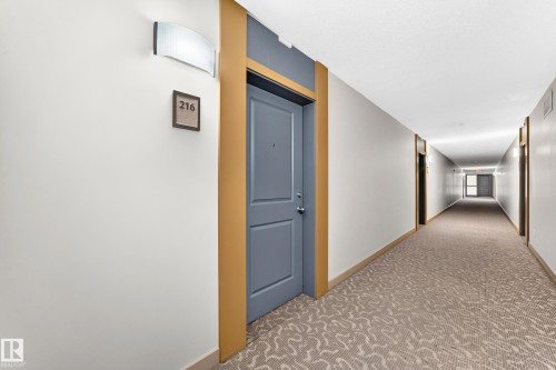 Corridor with patterned carpet flooring, modern wall sconce, and framed unit number 216 - #216 17003 67 Av Nw, Edmonton, AB - Indoor Photo Showing Other Room