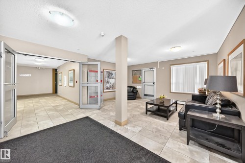 Travertine-style tile flooring throughout, multiple overhead light fixtures, and a glass-paneled entry door - #216 17003 67 Av Nw, Edmonton, AB - Indoor Photo Showing Other Room