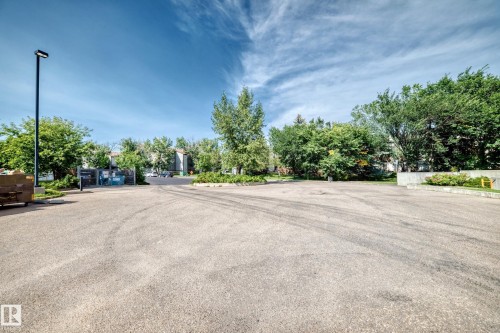 Paved parking area with established landscaping, perimeter fencing, and a modern light fixture - #216 17003 67 Av Nw, Edmonton, AB - Outdoor