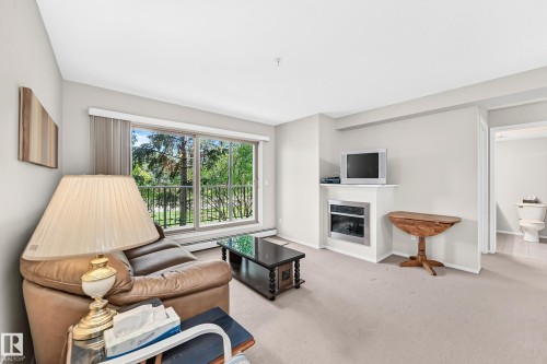 Expansive sliding glass doors, white fireplace surround with an insert, and light-toned carpeting - #216 17003 67 Av Nw, Edmonton, AB - Indoor Photo Showing Living Room With Fireplace