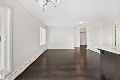 Spacious open-concept room featuring dark wood-finish flooring, white walls, and multiple windows - #318 5521 7 Av Sw Sw, Edmonton, AB - Indoor Photo Showing Other Room